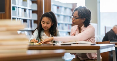 Tutor helps a female elementary school student study for a test. 